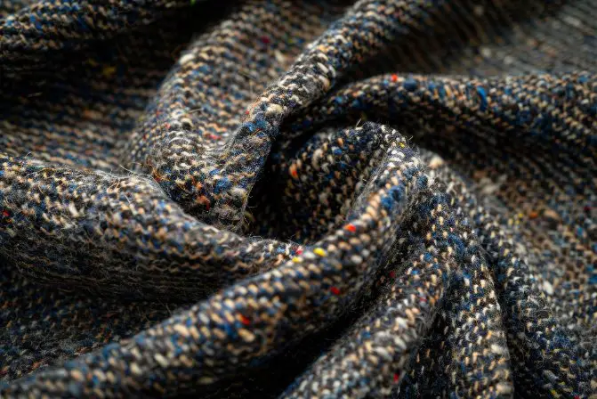 Close up of wool tweed fabric showing textured weave and multicolored fibers