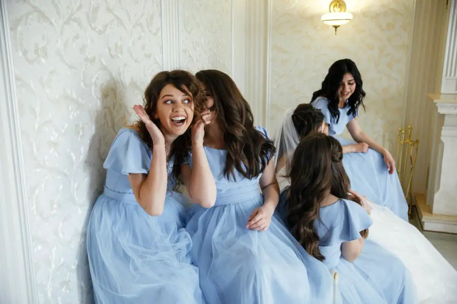 Girls wearing matching light blue junior bridesmaid dresses laughing together indoors