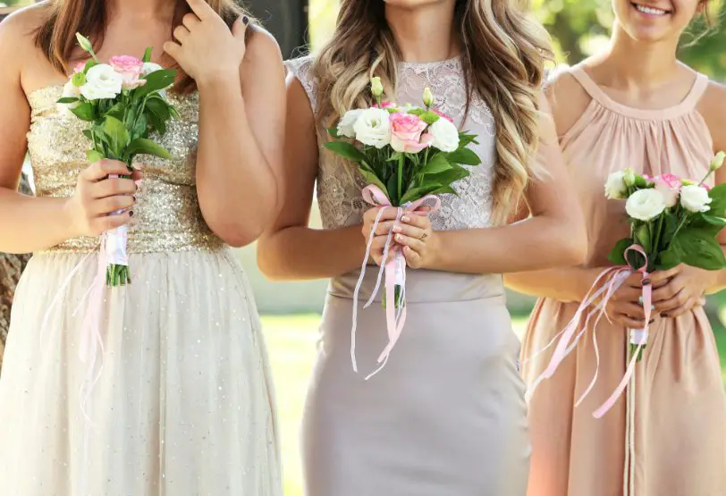 Junior bridesmaids holding flower bouquets and wearing coordinated pastel dresses outdoors