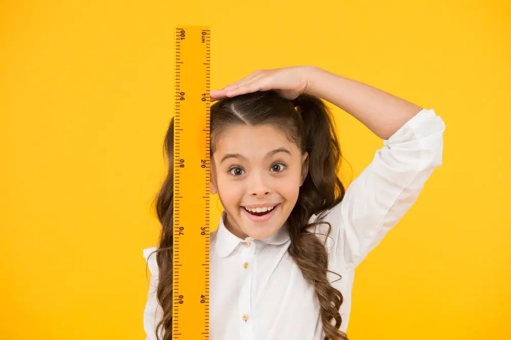 Smiling young girl measuring her height with a ruler for junior bridesmaid dress fitting