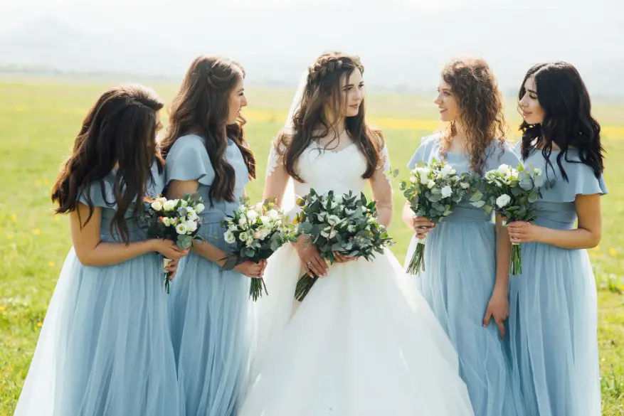 Bride standing with bridesmaids wearing matching light blue dresses in a field