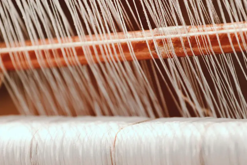 Close-up view of weaving threads on a loom representing how satin fabrics are constructed