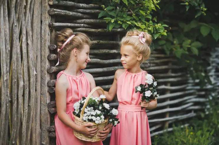 Two young girls wearing pink junior bridesmaid dresses holding flower baskets outdoors
