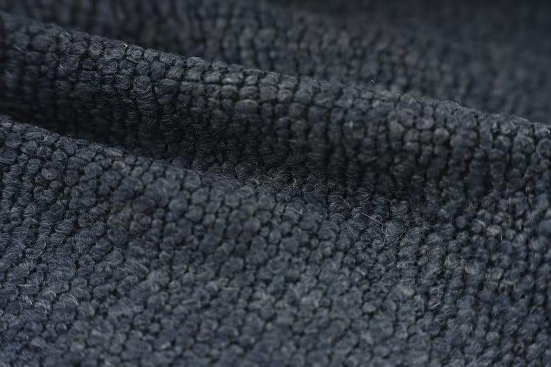 Close up of bouclé wool fabric showing looped texture, depth, and natural wool fibers.