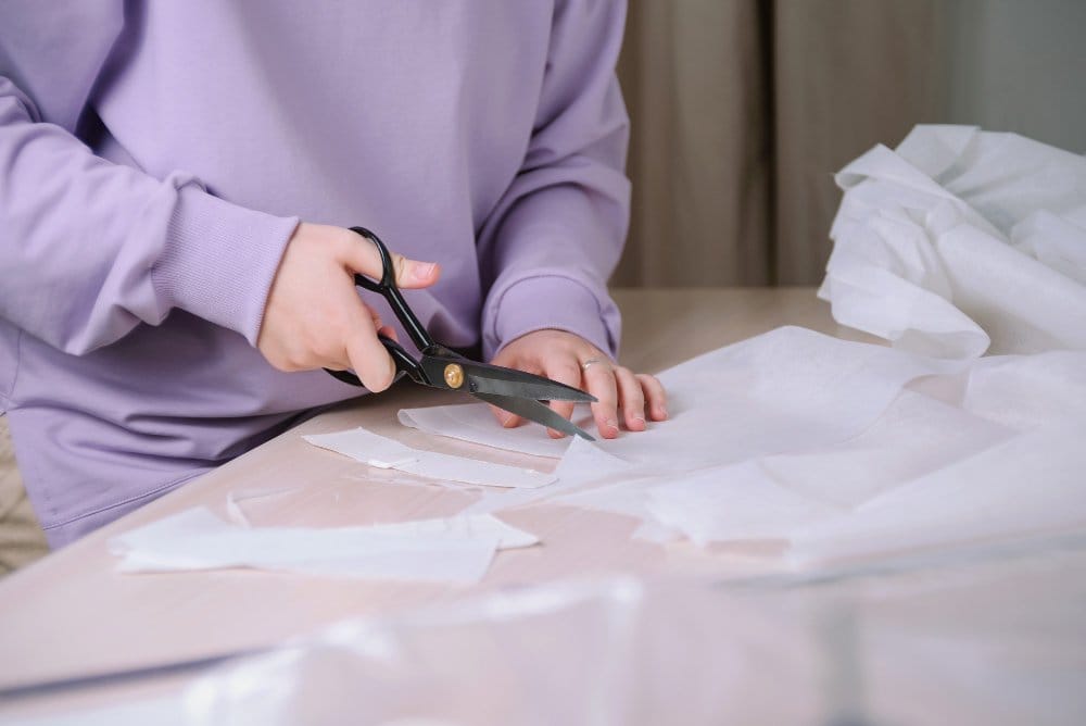 Hands carefully cutting chiffon fabric using fabric scissors on a flat surface