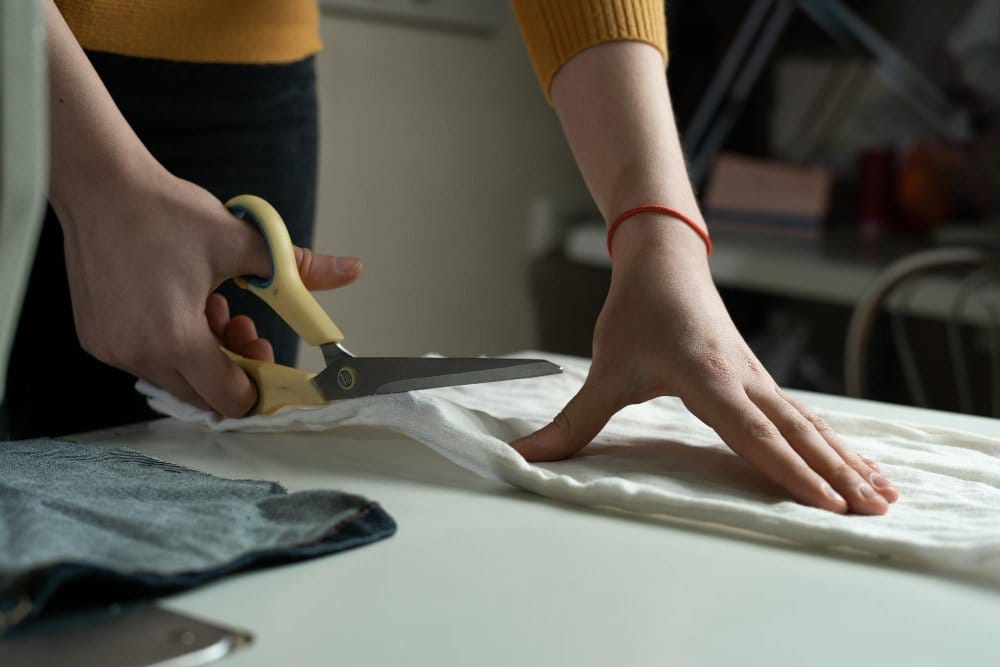 Cutting wool jersey fabric with scissors on a work table during garment preparation