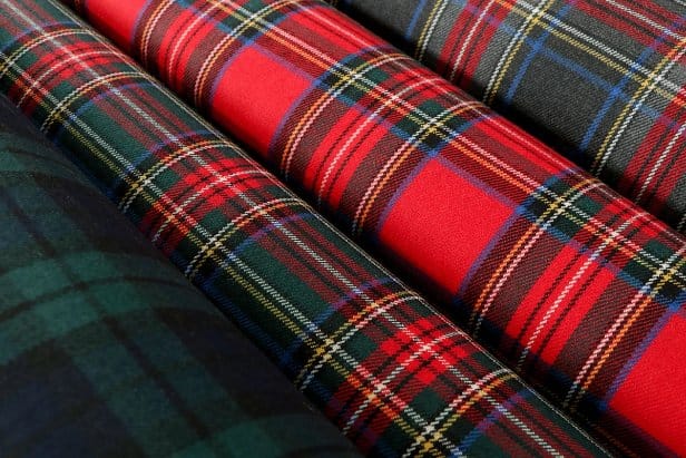 Rolled tartan wool fabrics in classic red, green, and navy plaid patterns displayed side by side