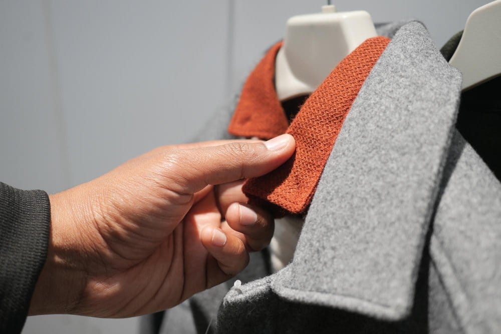 Person examining wool coats and fabrics in a retail store setting
