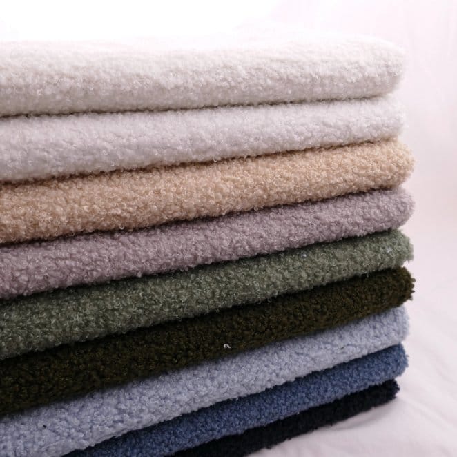 Stacked bouclé wool fabrics in multiple colors showing texture, thickness, and quality variation