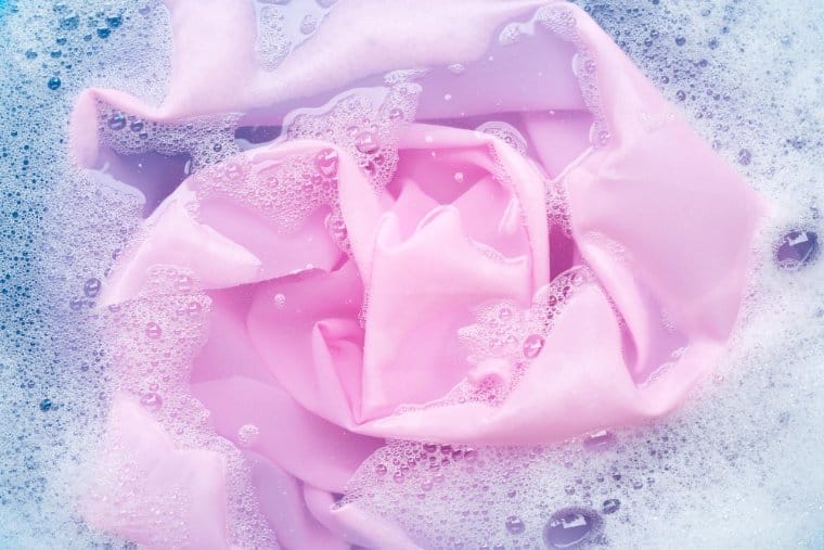 Pink chiffon fabric soaking in soapy water bubbles during gentle hand washing for delicate fabric care