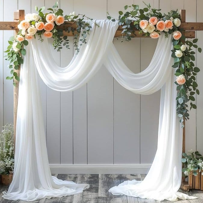 White nylon chiffon fabric draped over wooden wedding arch with flowers creating soft romantic event backdrop