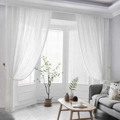 White nylon chiffon sheer curtains hanging by bright window allowing soft natural light into modern living room