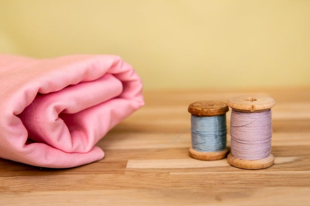 Folded wool broadcloth fabric with sewing thread spools on a wooden surface