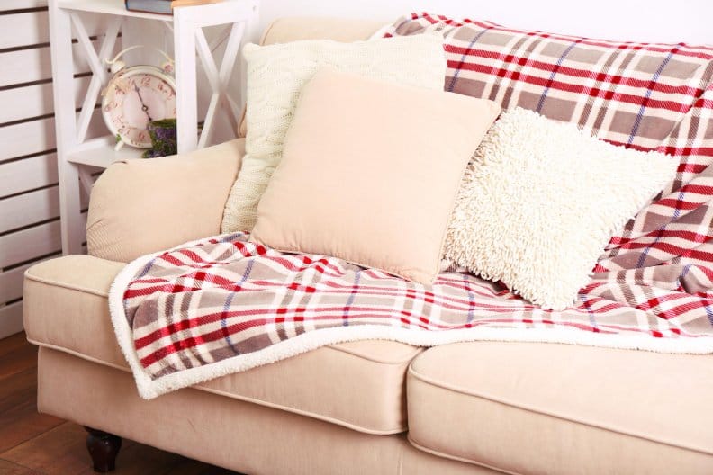 Tartan wool throw blanket draped over sofa with neutral cushions in cozy living room