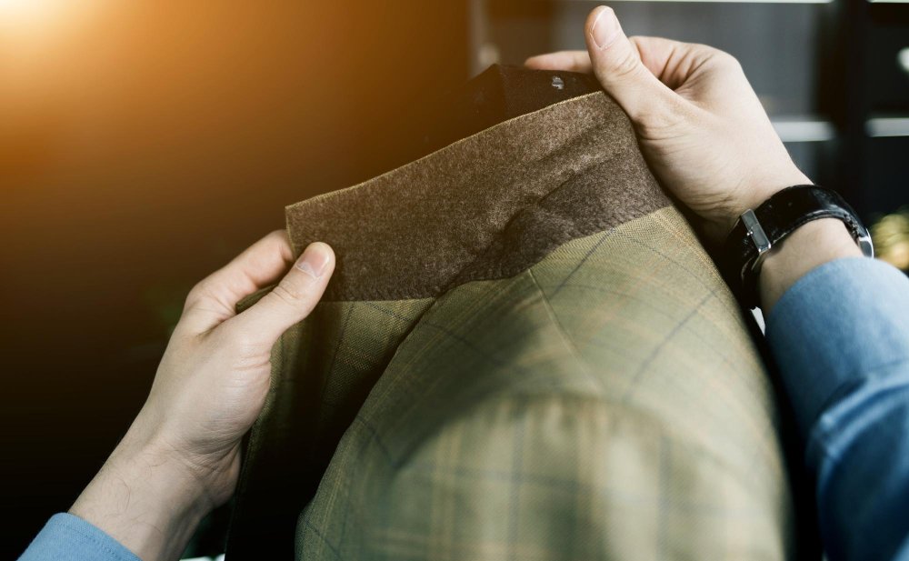 Hands inspecting the inside lining and seams of a wool sharkskin suit jacket to demonstrate proper care and maintenance