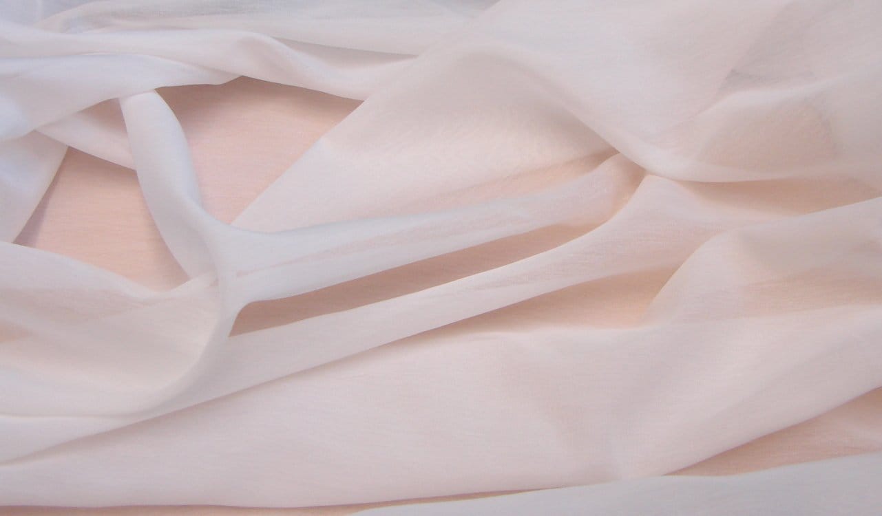 Soft beige cotton crepe chiffon fabric draped in flowing folds showing lightweight texture and slightly crinkled surface