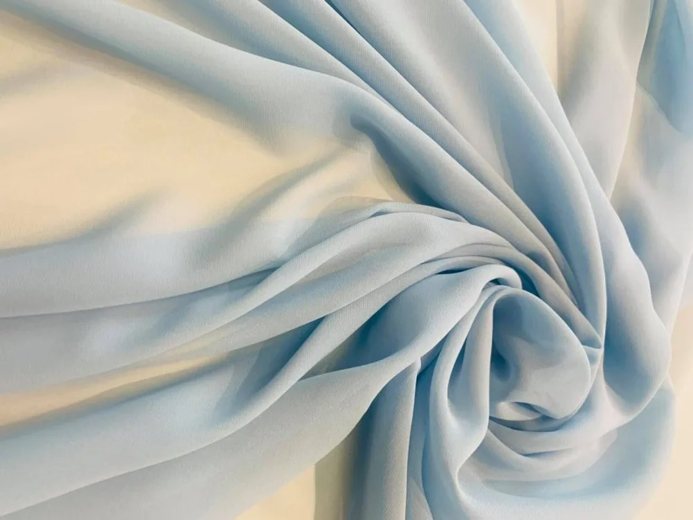 Light blue crepe chiffon fabric close up with twisted folds highlighting grainy crepe texture and flowing drape