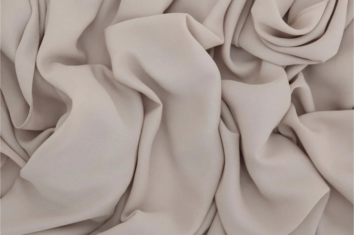 Close up of soft beige double face chiffon fabric spread out to show fine texture, semi sheer appearance, and fluid drape.