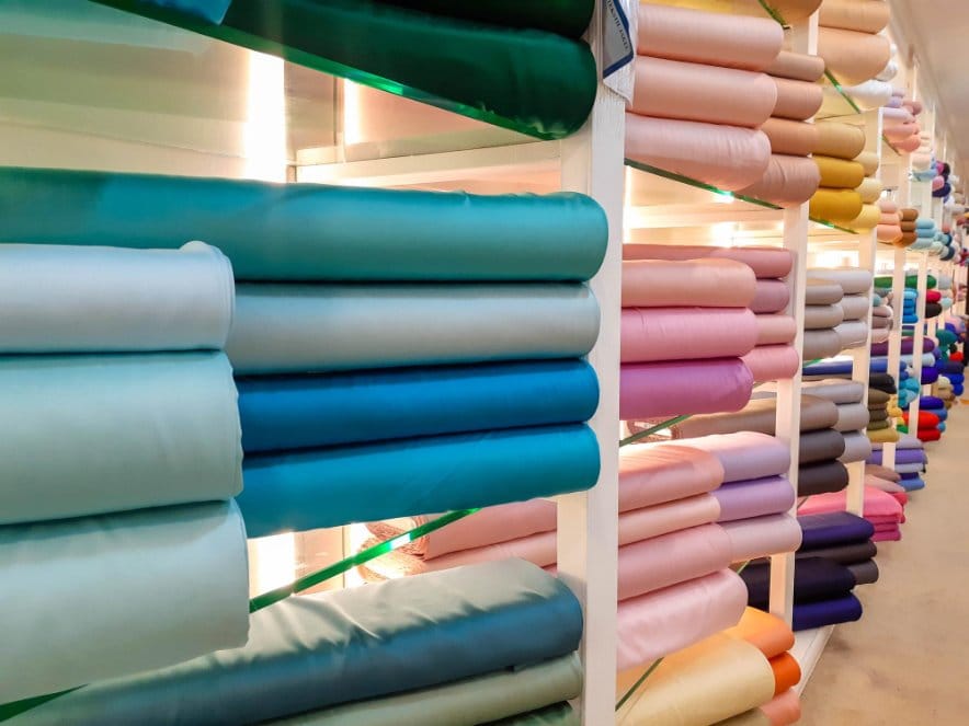 Bolts of colorful georgette chiffon fabric displayed on shelves in a textile store