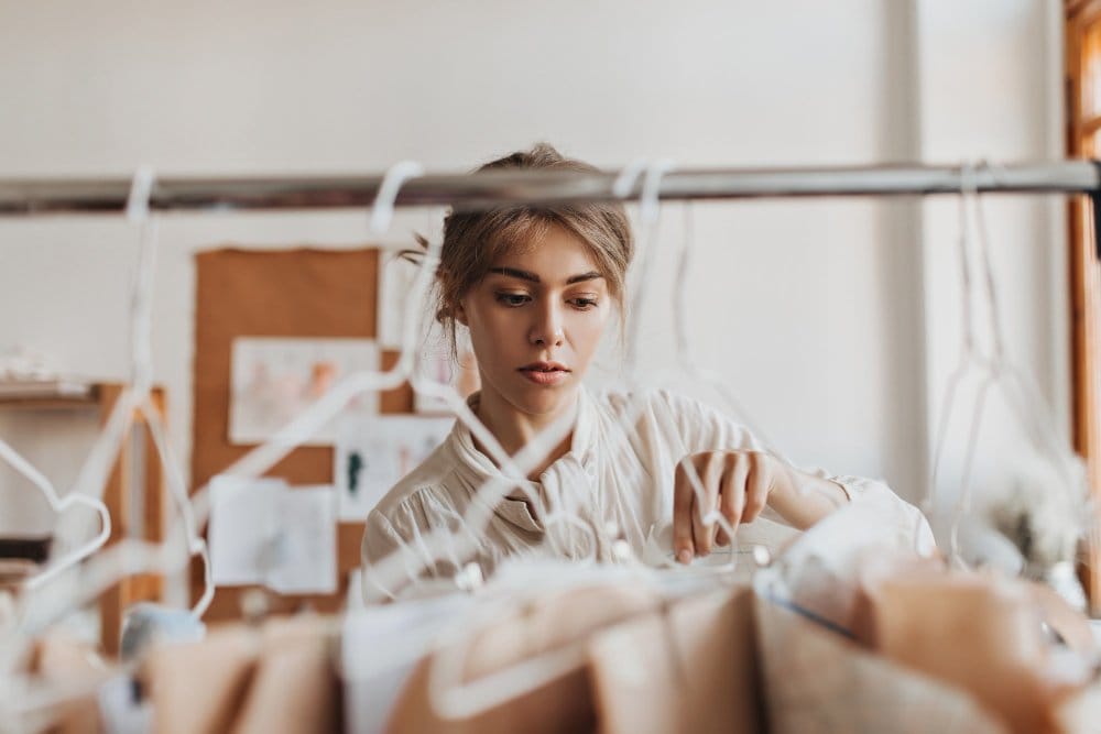 Fashion designer inspecting burnout chiffon fabric on clothing rack, choosing high quality sheer patterned textiles