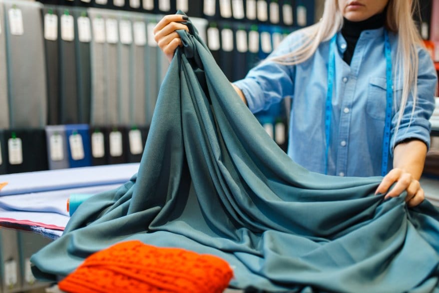 Person inspecting rayon chiffon fabric in a textile store to check drape, softness, and fabric quality