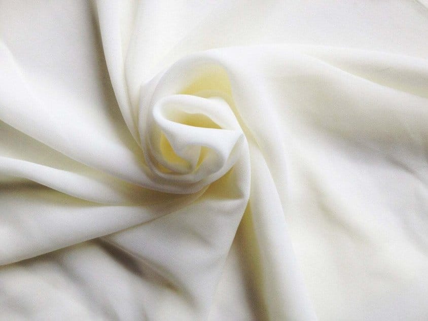 Cream colored polyester crepe chiffon fabric in soft folds showing lightweight sheer texture and wrinkle resistant drape