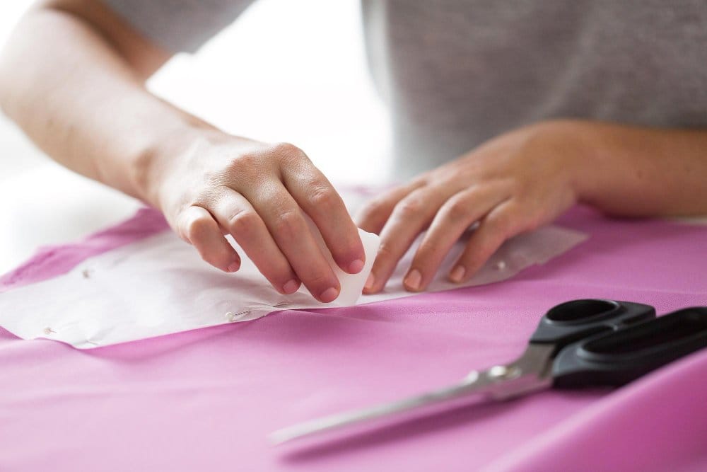 Hands cutting and pinning rayon chiffon fabric during sewing and pattern preparation