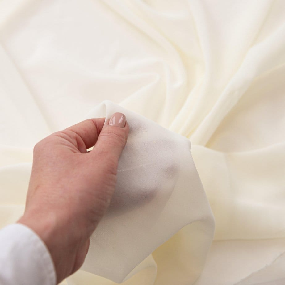 Hand holding cotton chiffon fabric to show softness, weave quality, and lightweight texture