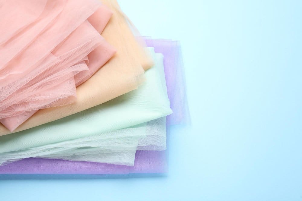Stack of pastel crepe chiffon fabrics folded neatly showing clean soft texture representing gentle washing and fabric care