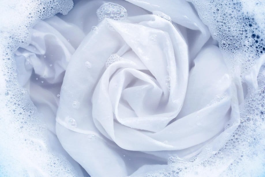 White pearl chiffon fabric soaking in soapy water with bubbles, illustrating gentle washing and fabric care