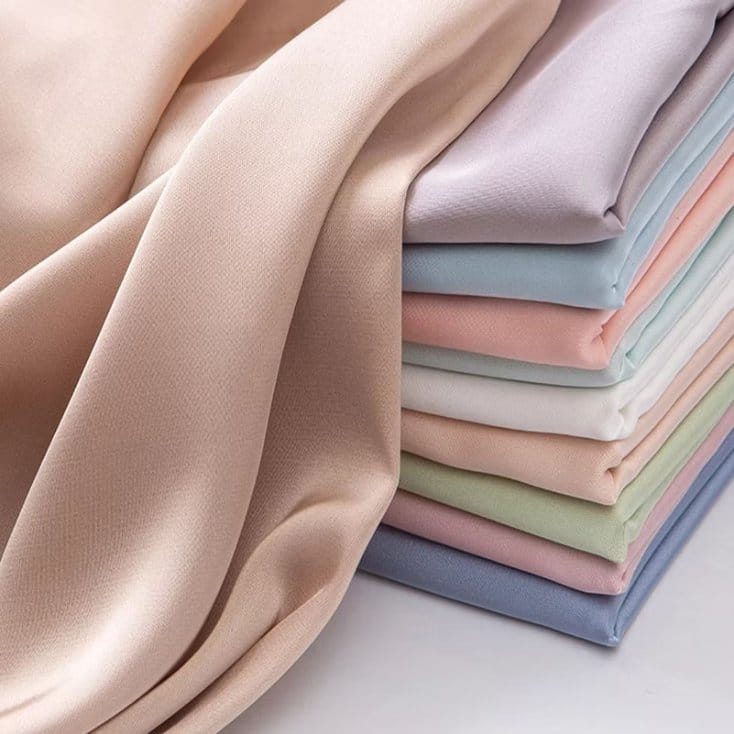 Stack of folded polyester chiffon fabrics in pastel colors showing smooth texture drape and color options for sewing projects