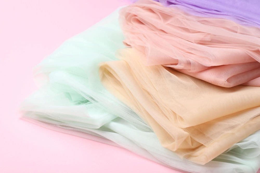 Layered pastel chiffon fabrics arranged on pink background representing gentle washing drying and fabric care practices