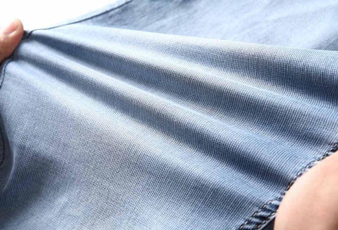 Close up of stretch denim fabric being pulled to demonstrate elasticity and flexibility in jeans material