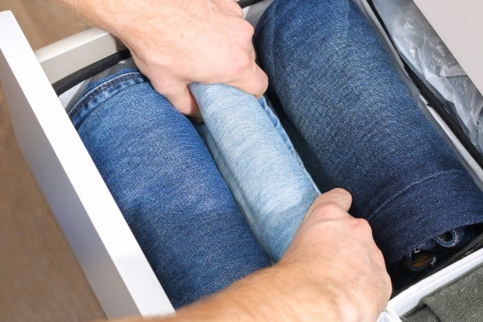 Hands folding stretch denim jeans into a drawer showing proper storage and care for maintaining elasticity