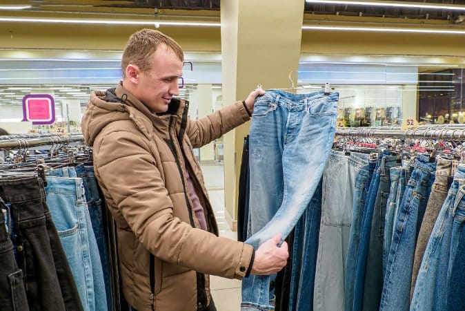 Checking a pair of jeans in a store to identify washed denim by color, fade, and finish. Man in a clothing store examining light blue jeans on a rack to identify washed denim finishes.