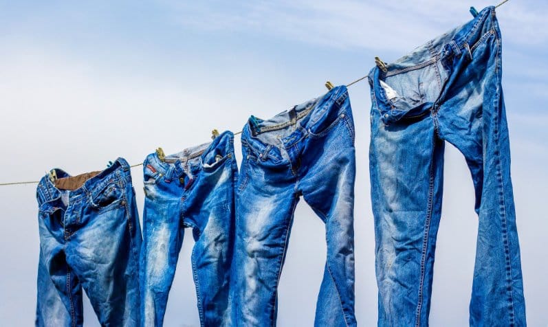 Blue jeans hanging on a clothesline outdoors, illustrating natural drying and care for 100% cotton denim.