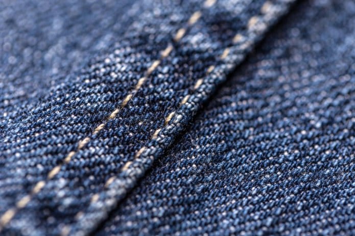 Macro close-up of raw denim seam and twill weave showing stitching, texture, and fabric construction details.