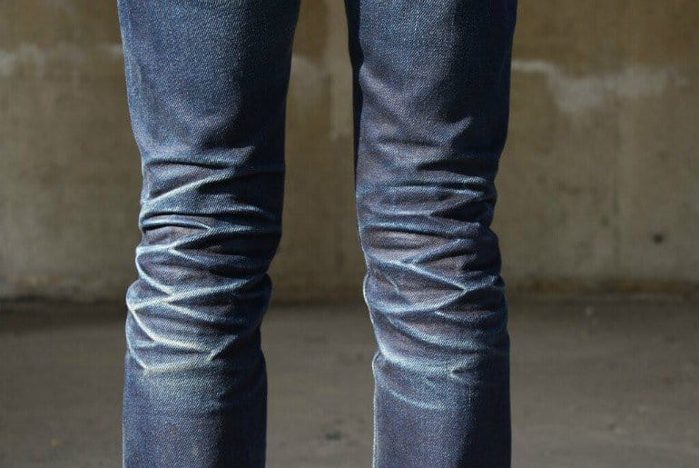 Close-up of faded denim jeans showing whiskers and honeycomb creases formed through wear over time.