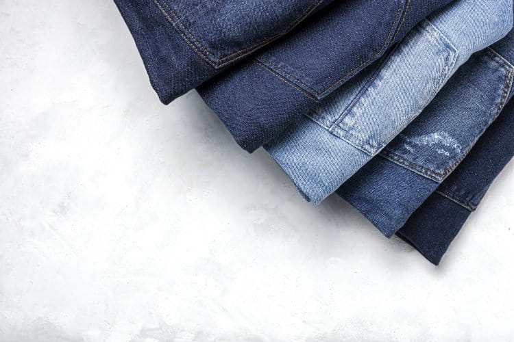 Stacked folded jeans in different washes arranged on a light surface, representing variety in denim construction and quality.