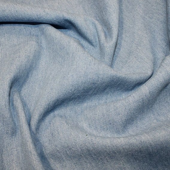 Washed denim fabric close-up showing a soft hand feel and light faded blue appearance. Close-up of light blue washed denim fabric with soft folds and a smooth faded texture.