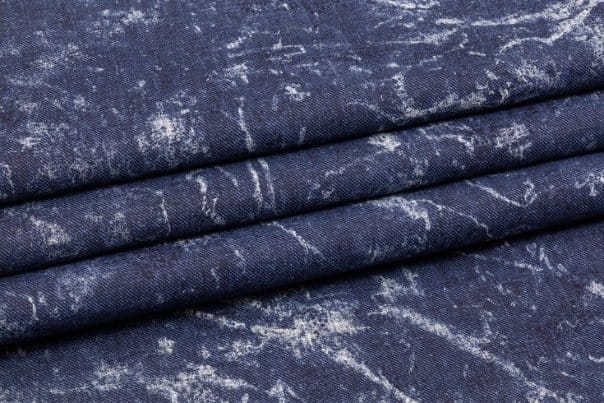 Dark blue acid washed denim fabric with marbled faded patterns and textured surface detail.