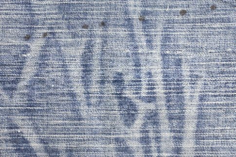 Laser washed denim fabric with pale faded streaks and linear patterns across a blue woven surface.