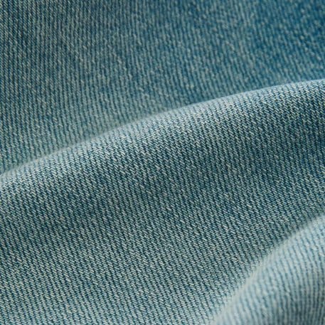 Light blue stone washed denim fabric with soft folds and a worn, faded casual finish.