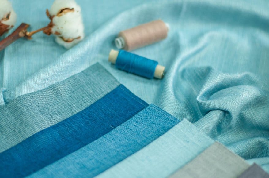 Selection of blue chambray fabric swatches with sewing thread and cotton bolls, showcasing chambray as a versatile fabric for sewing projects.
