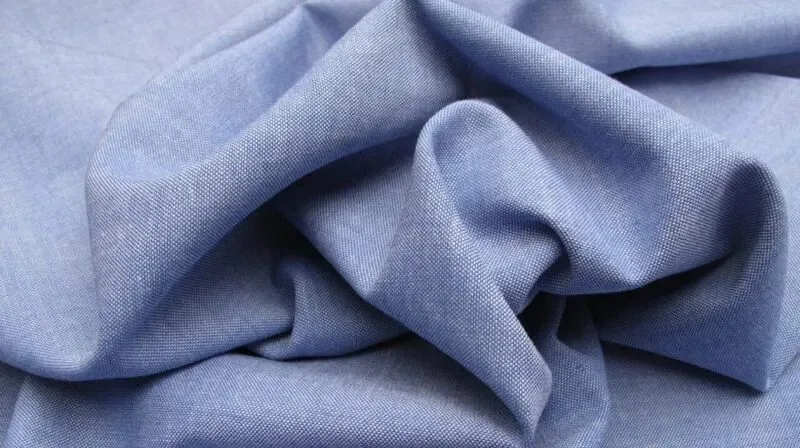 Close-up of soft blue chambray fabric showing its smooth texture, lightweight drape, and finely woven construction.