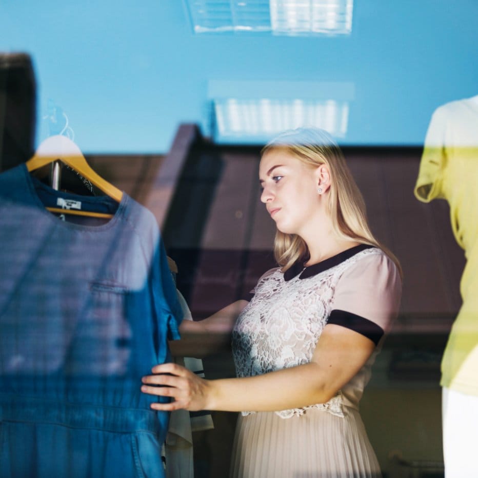 Shopper examining blue chambray clothing in a retail store while selecting fabric or garments made from chambray.