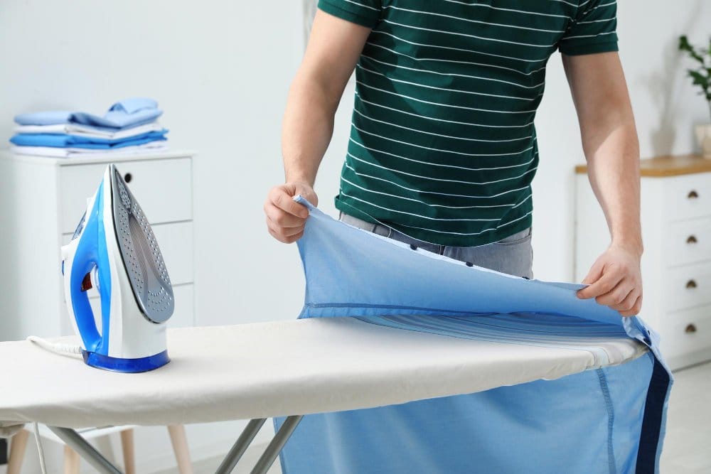 Person pressing a blue chambray garment on an ironing board, demonstrating the importance of pressing during garment construction.