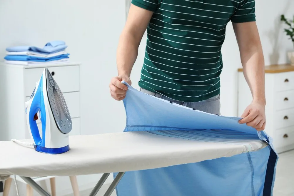 Person pressing a blue chambray garment on an ironing board, demonstrating the importance of pressing during garment construction.