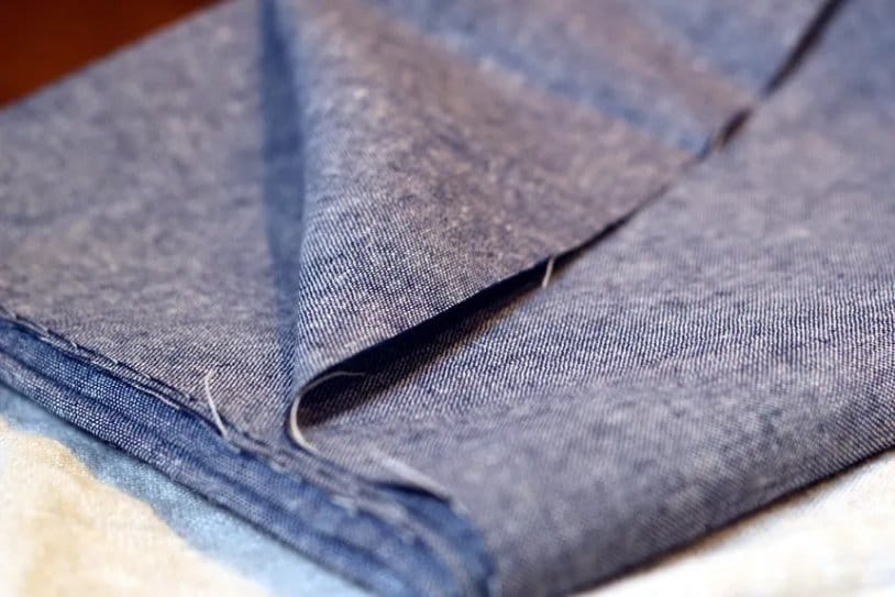 Close-up of folded blue chambray fabric showcasing the traditional woven construction associated with the history of chambray.