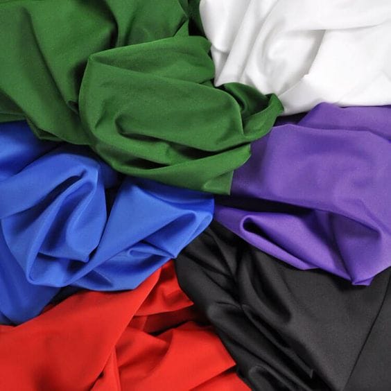 Assorted nylon spandex fabrics in multiple colours representing textile production and manufacturing processes.